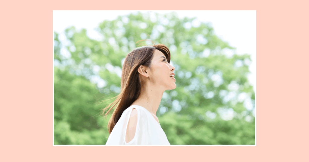 白いトップスを着て笑顔で空を見上げる50代女性の横顔。明るく前向きな印象。